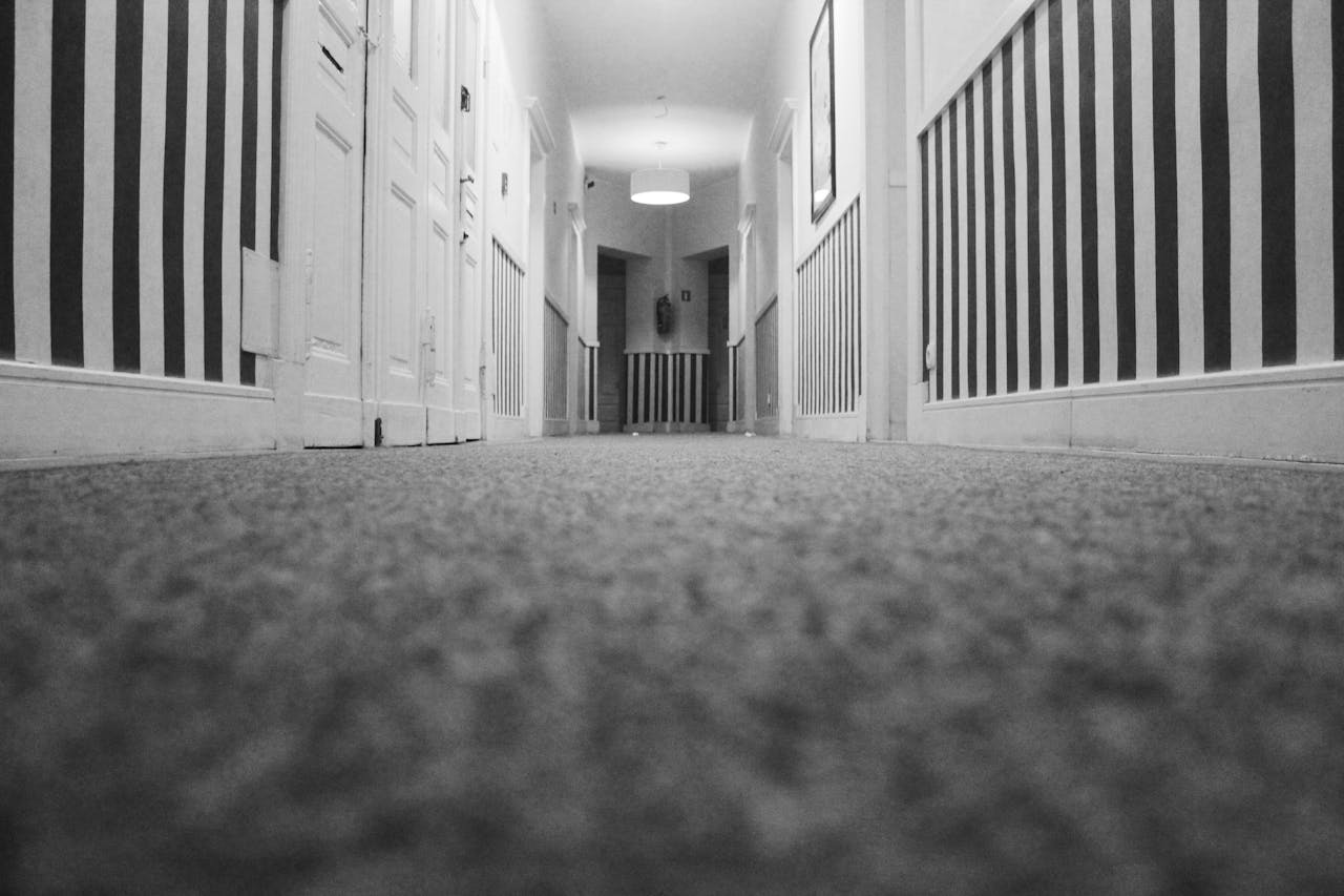 services-01 Low angle view of an empty hotel corridor with striped walls and carpet in monochrome.